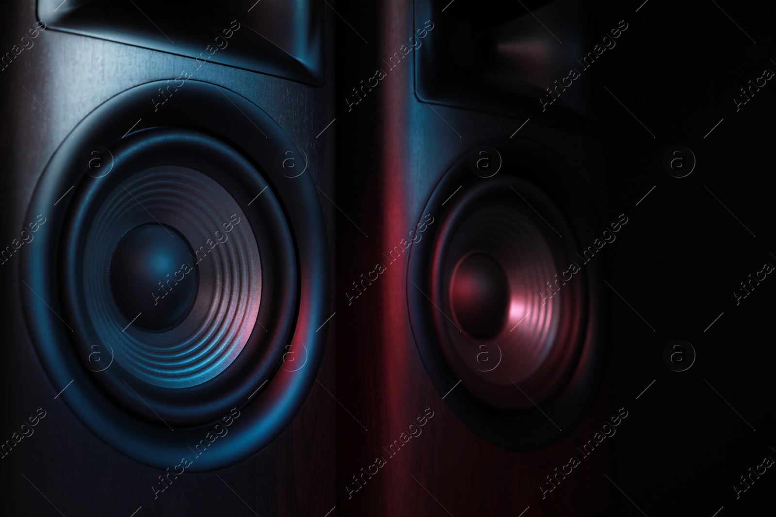 Photo of Modern sound speakers in neon light on black background, closeup