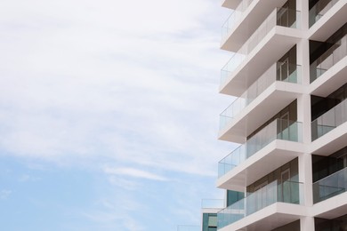 Photo of Exterior of residential building with balconies against blue sky, low angle view. Space for text