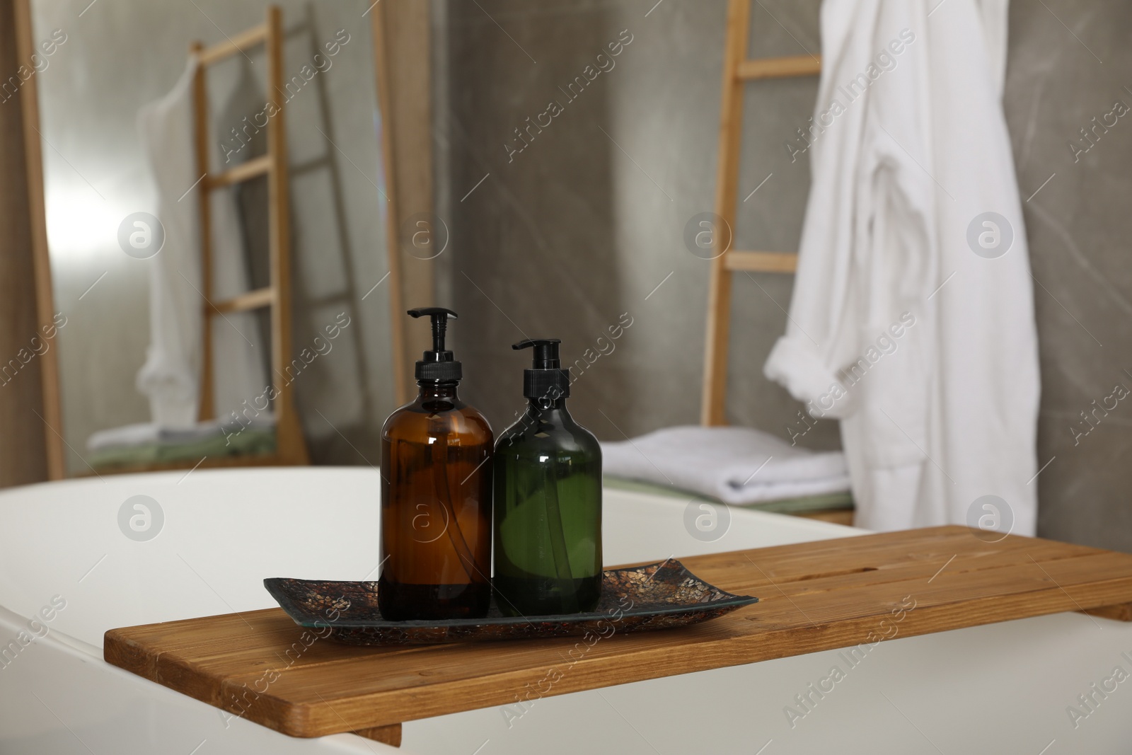 Photo of Wooden bath tray with bottles of shower gels on tub indoors, space for text
