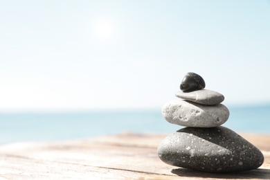 Photo of Stack of stones on wooden pier near sea, space for text. Zen concept