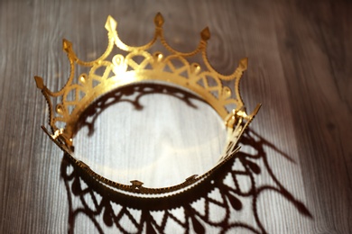 Photo of Beautiful golden crown with gems on wooden table. Fantasy item