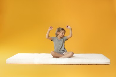 Little girl waking up on mattress against orange background