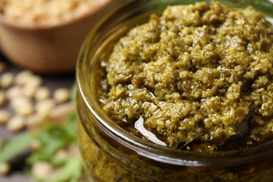 Photo of Jar of tasty arugula pesto on table, closeup