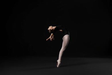 Photo of Young ballerina practicing dance moves on black background