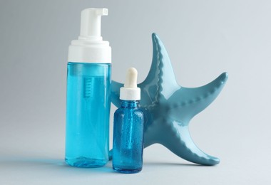 Bottles of cosmetic products and decorative starfish on light grey background