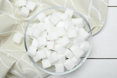 Many sugar cubes in glass bowl on white wooden table, top view