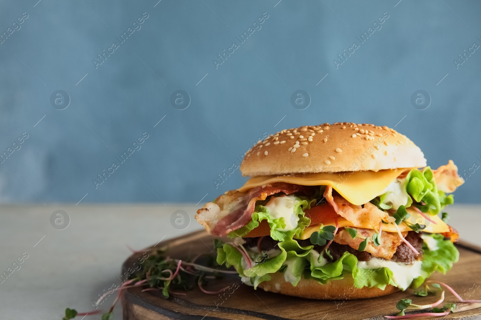 Photo of Tasty burger with bacon on board against color background. Space for text