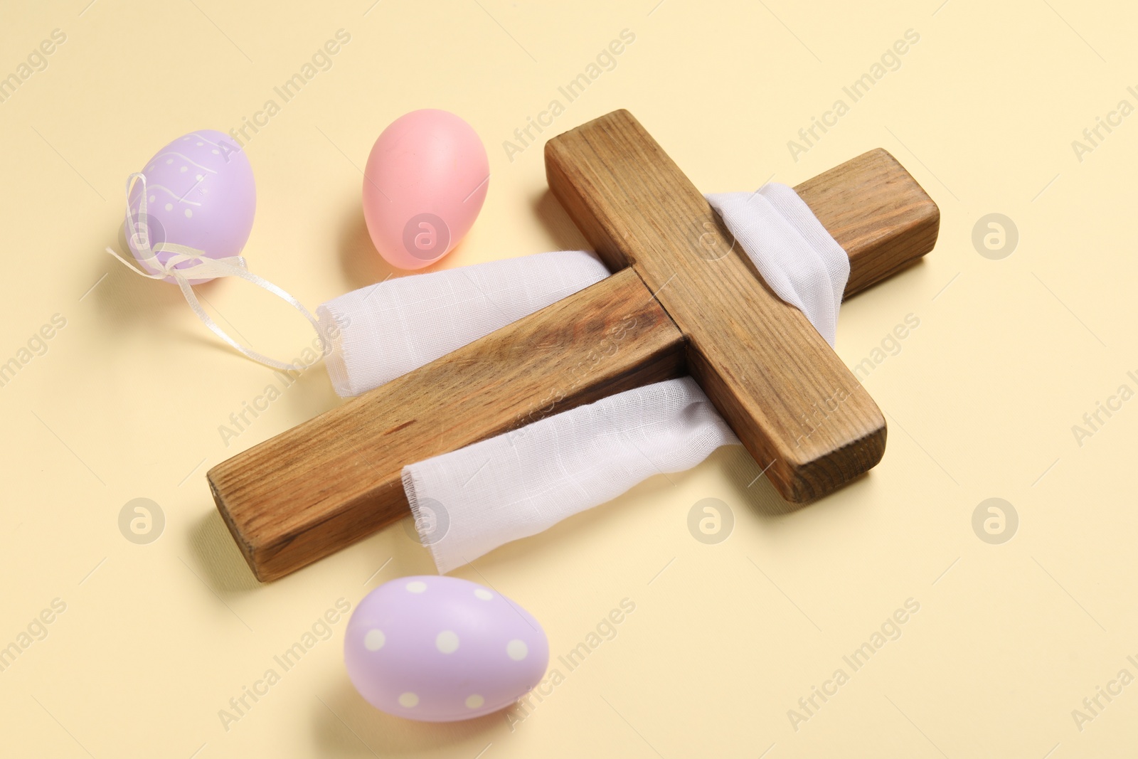 Photo of Wooden cross, white cloth and painted Easter eggs on beige background