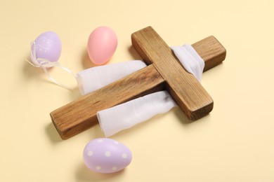 Wooden cross, white cloth and painted Easter eggs on beige background