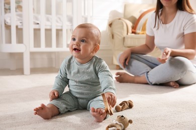 Cute baby girl playing with wooden toys and mother on floor at home