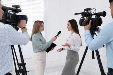 Photo of Professional journalist interviewing young business woman and cameramen shooting video for broadcast