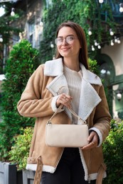 Fashionable young woman with stylish bag on city street