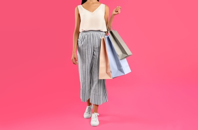 Young woman with paper shopping bags on pink background, closeup