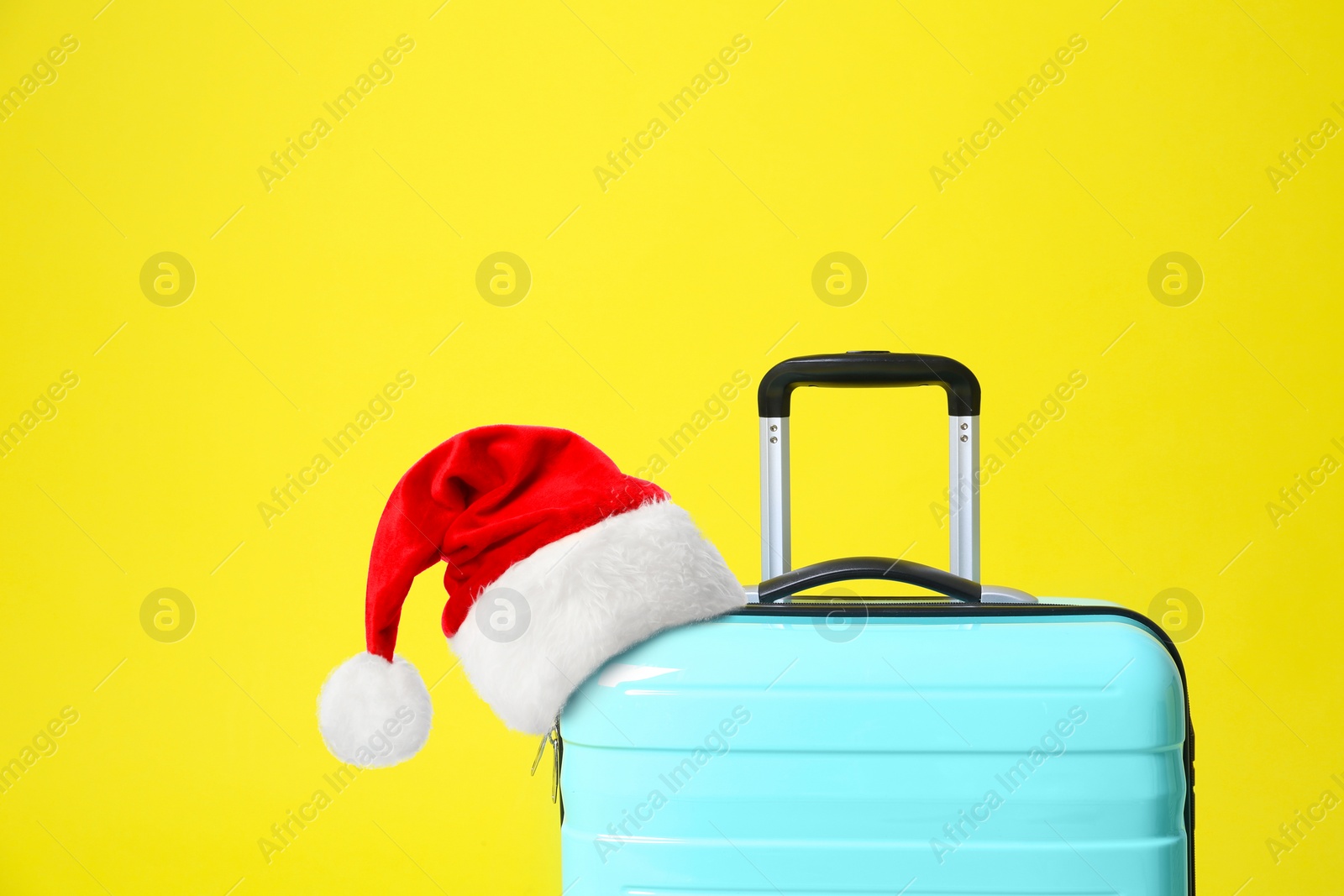 Image of Stylish suitcase with Santa Claus hat on yellow background. Christmas vacation 