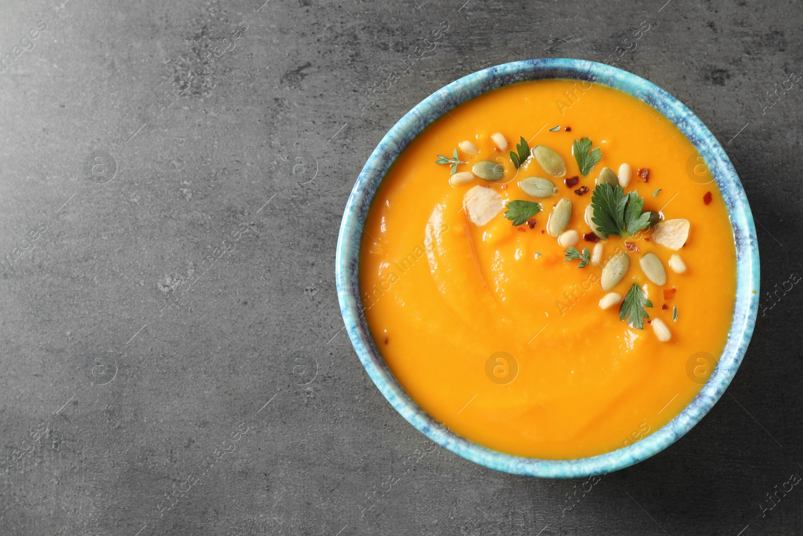 Photo of Delicious pumpkin soup in bowl on grey table, top view. Space for text