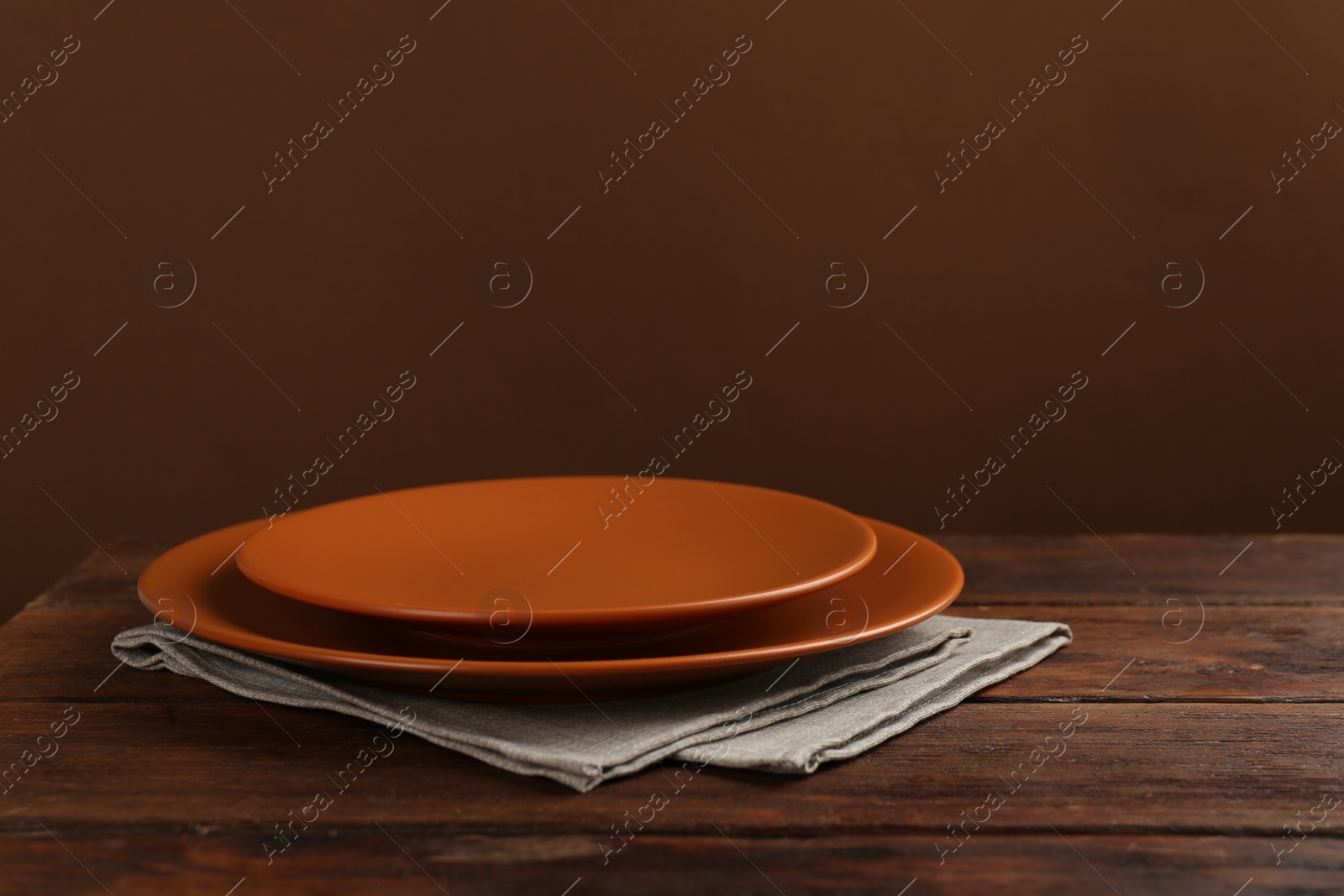 Photo of Beautiful ceramic plates and napkin on wooden table against brown background, space for text