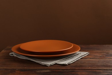 Photo of Beautiful ceramic plates and napkin on wooden table against brown background, space for text