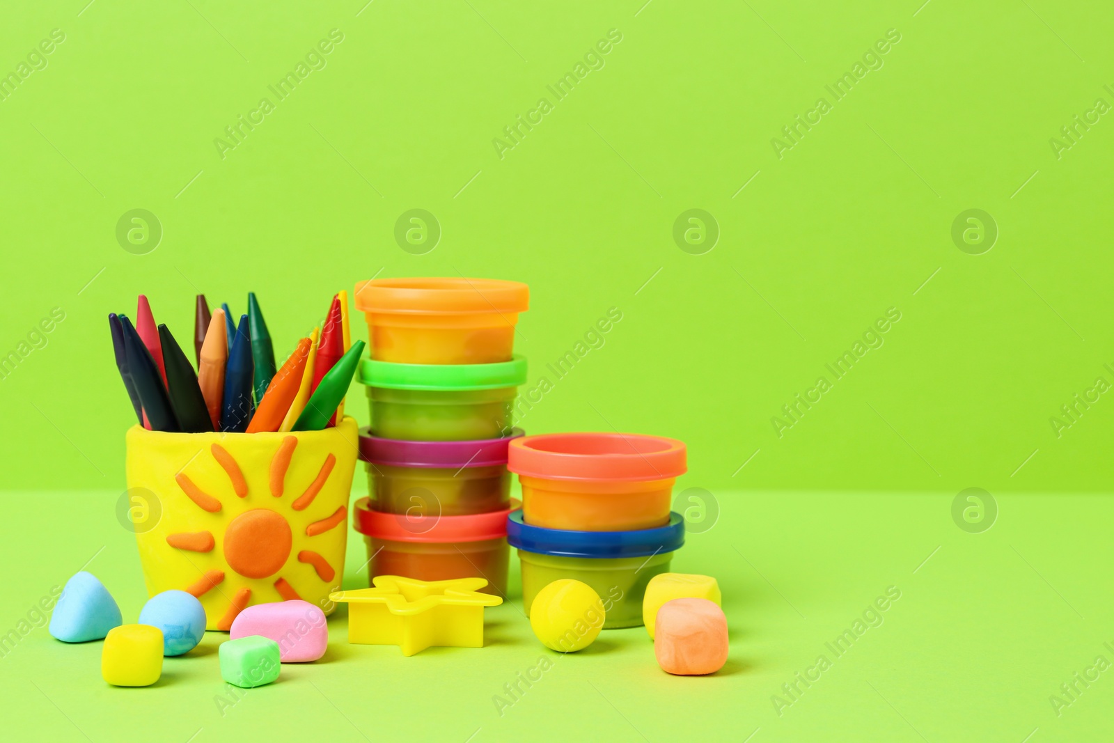 Photo of Set of bright play dough with mold and colorful pencils on light green background. Space for text