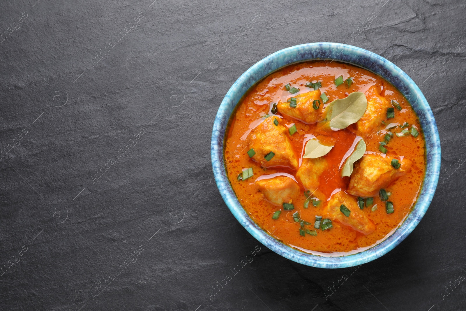 Photo of Bowl of delicious chicken curry on black table, top view. Space for text