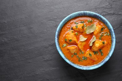 Bowl of delicious chicken curry on black table, top view. Space for text