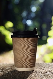 Photo of Cardboard takeaway coffee cup with plastic lid on stone parapet outdoors