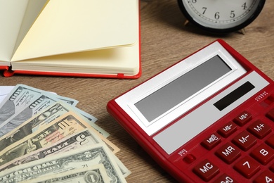 Photo of Calculator, notebook, money and alarm clock on wooden table, closeup. Tax accounting