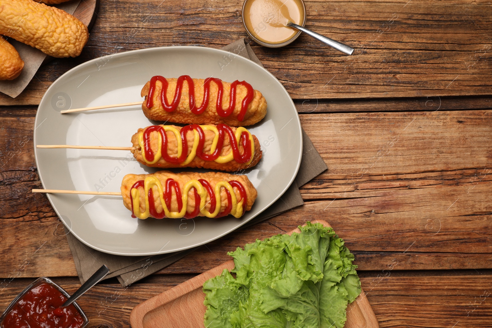 Photo of Delicious corn dogs with mustard and ketchup served on wooden table, flat lay