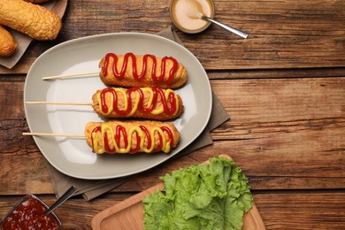 Delicious corn dogs with mustard and ketchup served on wooden table, flat lay