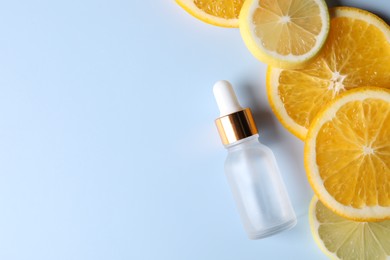 Photo of Bottle of cosmetic serum and sliced citrus fruits on light blue background, flat lay. Space for text
