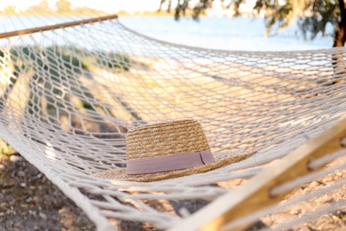 Photo of Hat in comfortable hammock on beach, closeup. Summer vacation