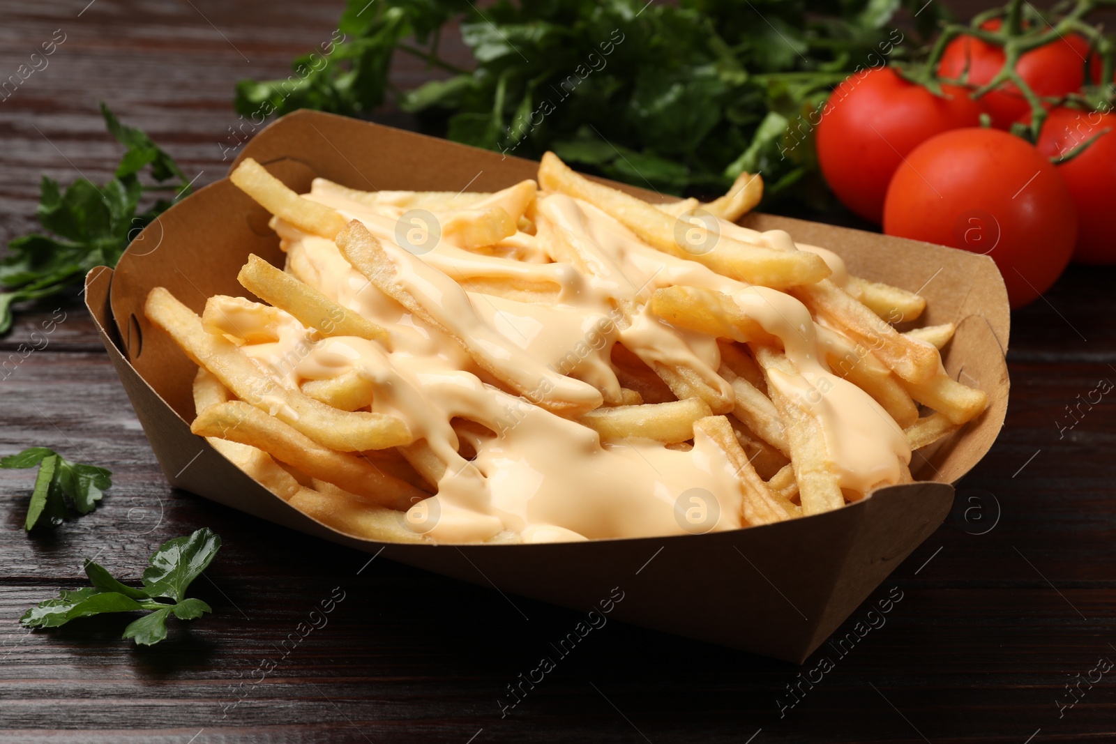 Photo of Tasty potato fries, cheese sauce in paper container and products on wooden table, closeup