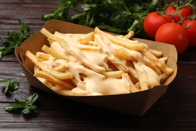 Tasty potato fries, cheese sauce in paper container and products on wooden table, closeup