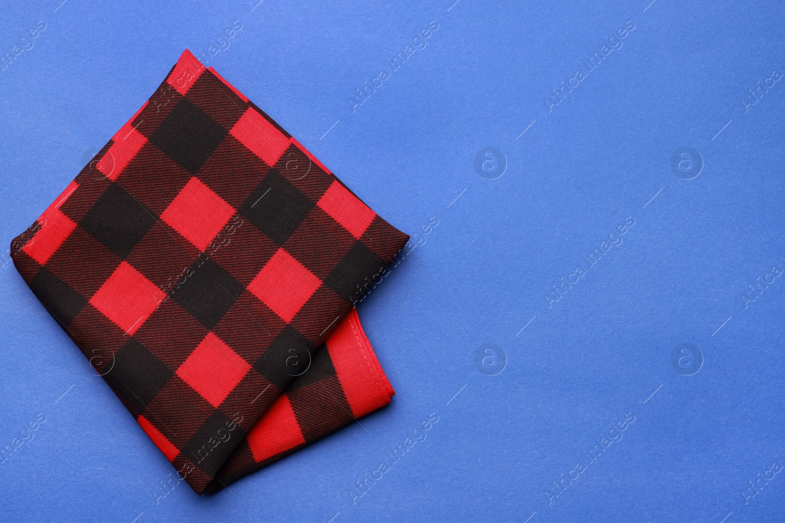 Photo of Folded red bandana with check pattern on blue background, top view. Space for text
