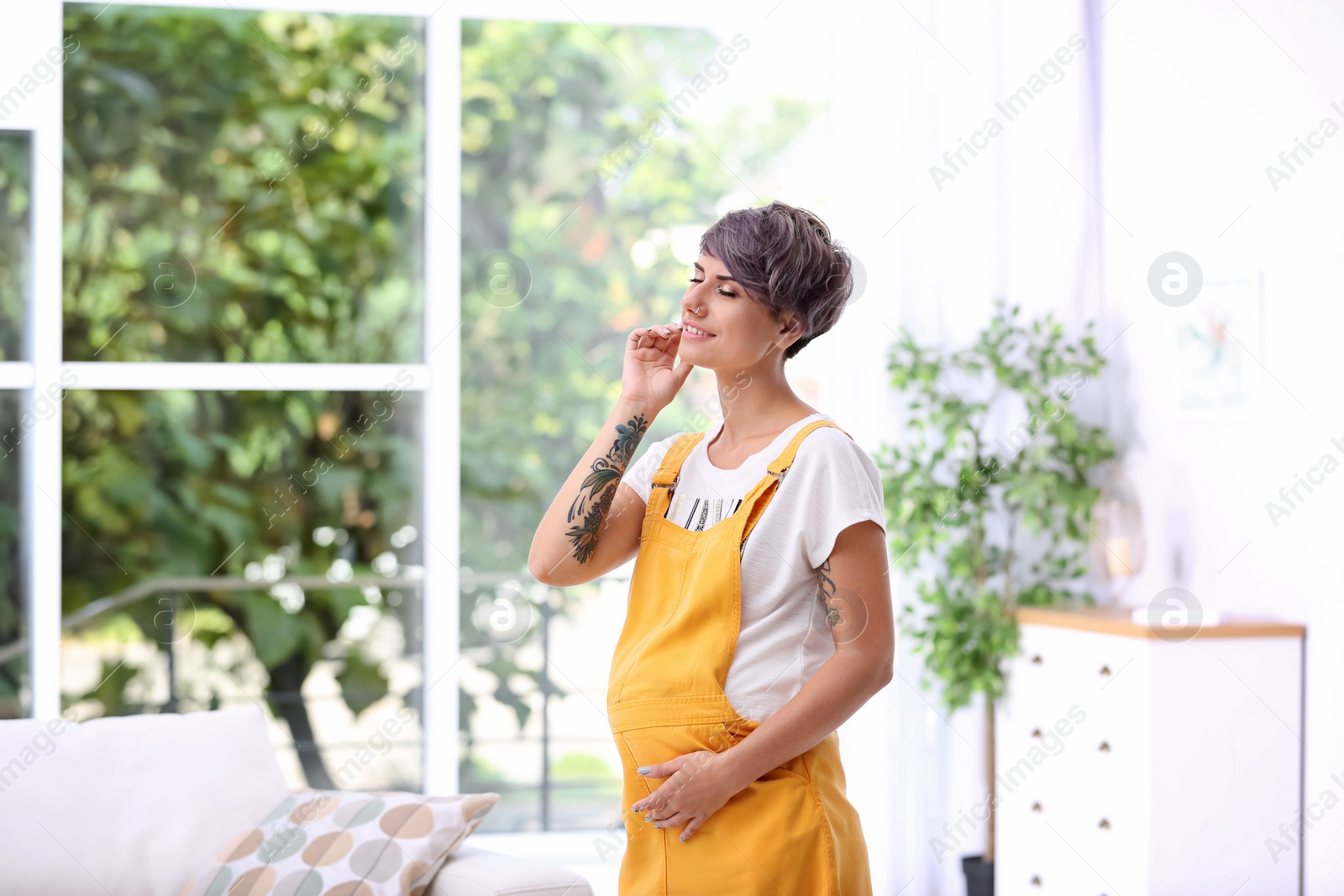 Photo of Trendy pregnant woman with tattoos standing indoors