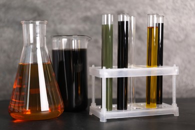 Photo of Test tubes, beaker and flask with different types of oil on grey table