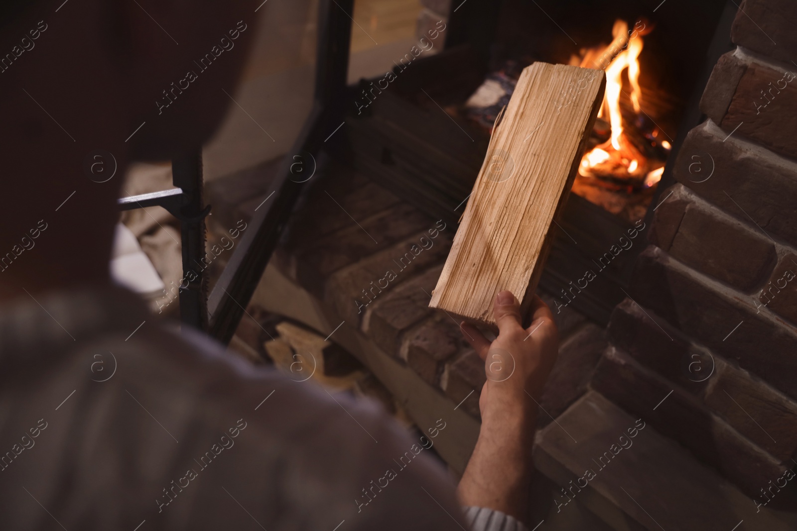 Photo of Man putting dry firewood into fireplace at home, closeup. Winter vacation