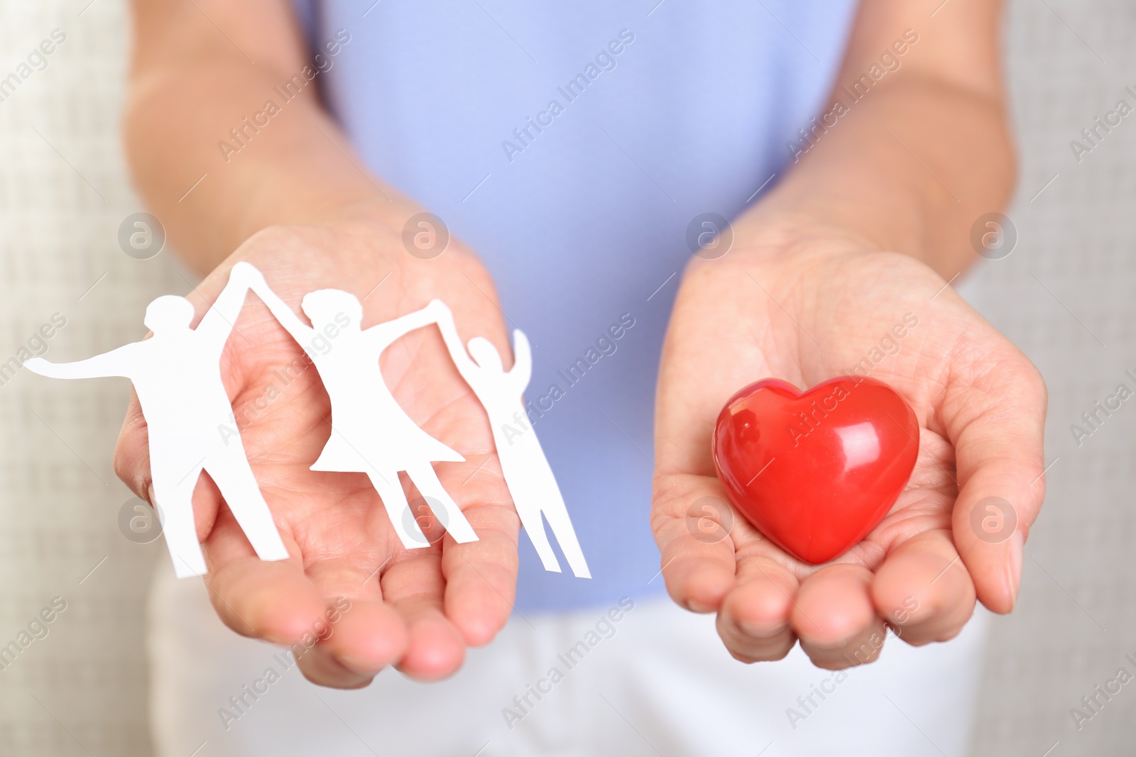 Photo of Young woman holding paper family figure and red heart, closeup of hands