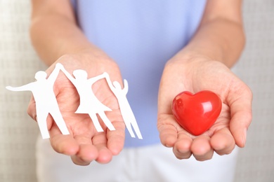 Photo of Young woman holding paper family figure and red heart, closeup of hands