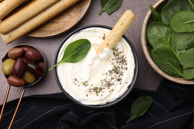 Photo of Delicious cream cheese with grissini stick, basil and olives on grey table, flat lay