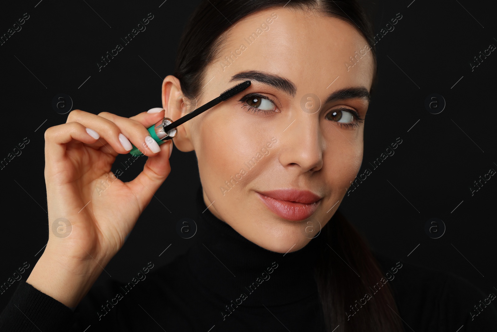 Photo of Beautiful young woman applying mascara on black background, closeup