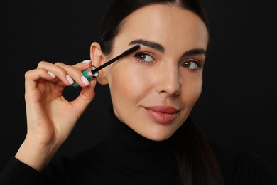 Photo of Beautiful young woman applying mascara on black background, closeup