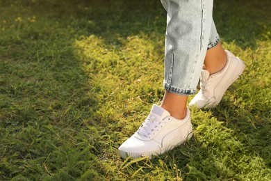 Photo of Woman in jeans and white shoes walking on green grass, closeup. Space for text