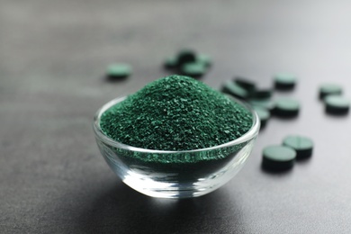 Photo of Bowl of spirulina algae powder on table near pills