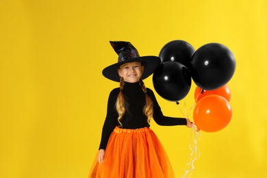Photo of Cute little girl with balloons wearing Halloween costume on yellow background