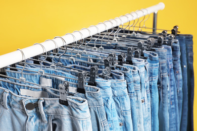 Rack with different jeans on yellow background, closeup