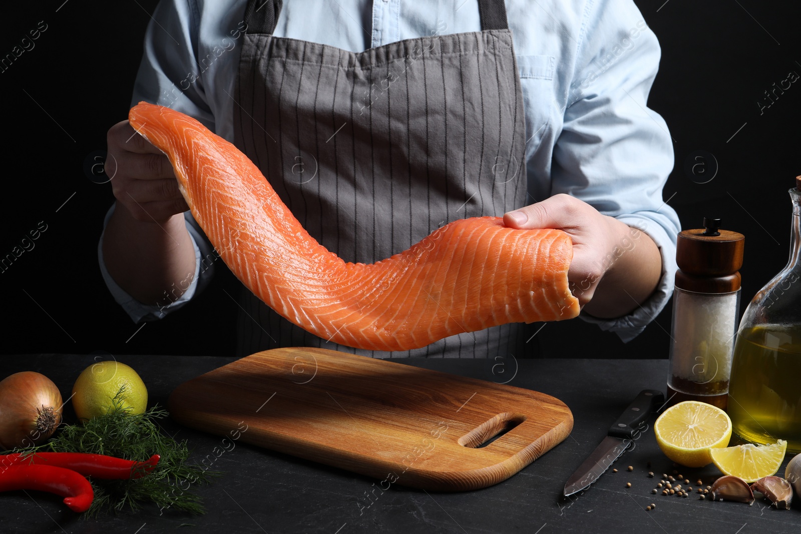 Photo of Man with raw salmon fillet at black table, closeup