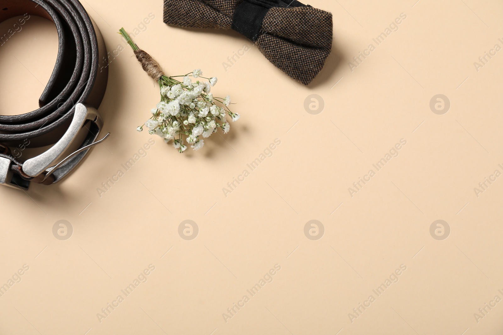 Photo of Wedding stuff. Stylish boutonniere, bow tie and belt on beige background, flat lay. Space for text