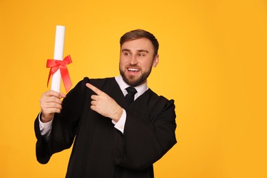 Happy student with diploma on yellow background