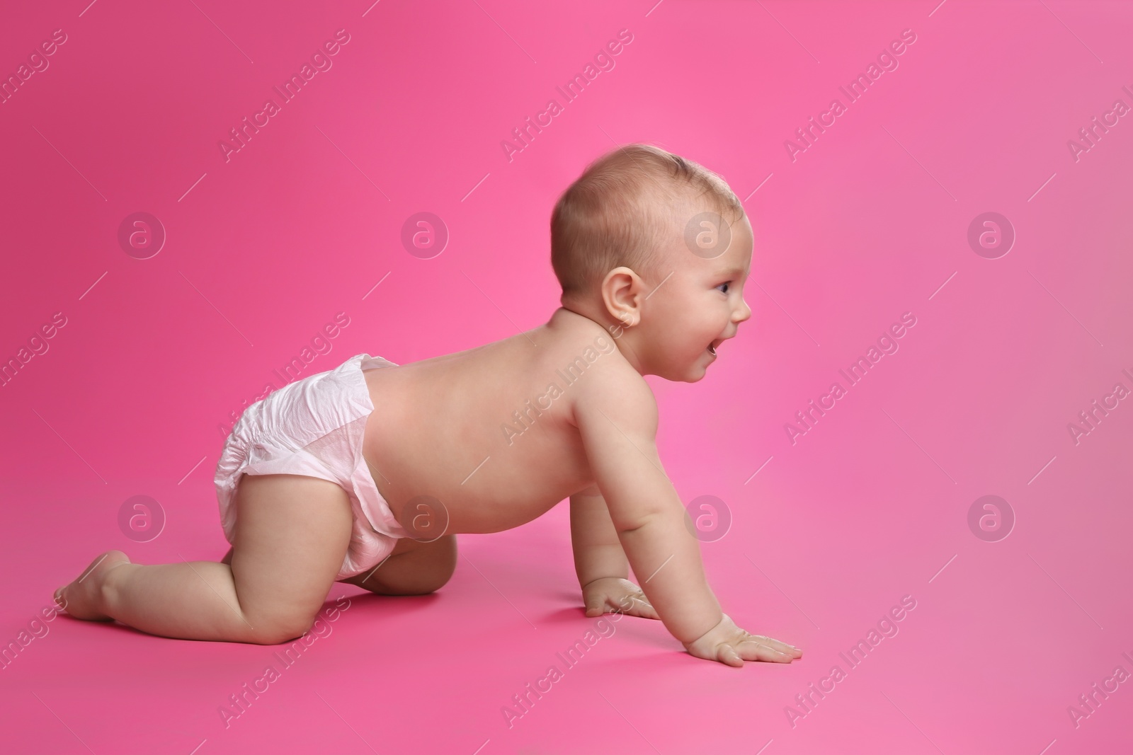 Photo of Cute baby in dry soft diaper crawling on pink background