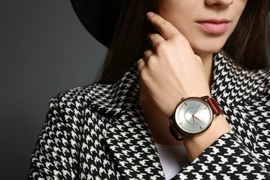 Woman wearing luxury wristwatch on grey background, closeup